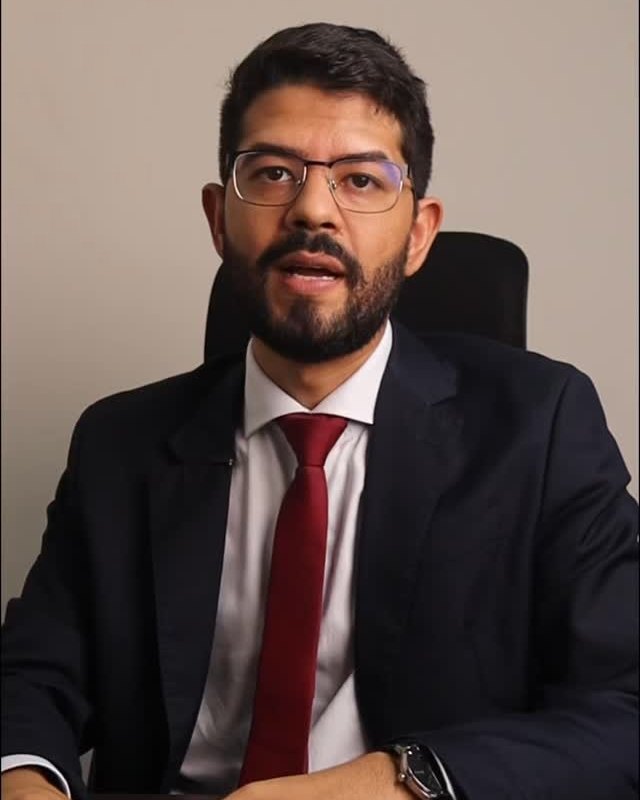 O advogado João Felipe de Sá, de terno e gravata vermelha, à mesa do escritório